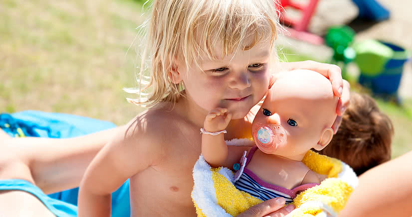 Mädchen kuschelt mit ihrer Puppe in der Sonne